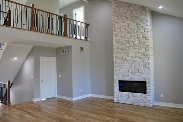 unfurnished living room with a high ceiling, wood finished floors, a stone fireplace, and visible vents
