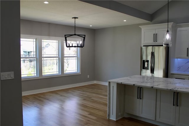 kitchen featuring baseboards, stainless steel fridge, a notable chandelier, wood finished floors, and light stone counters