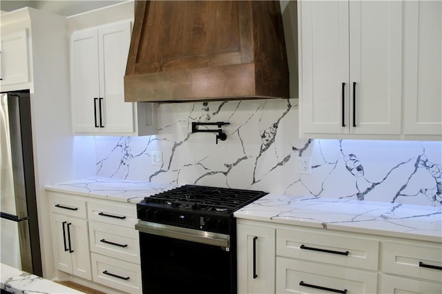 kitchen with custom range hood, white cabinets, freestanding refrigerator, and black gas range oven