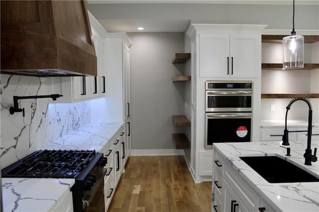 kitchen with custom range hood, open shelves, black gas range oven, stainless steel double oven, and a sink