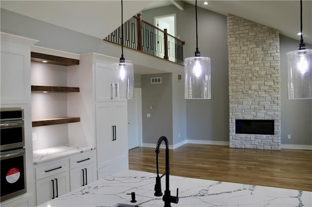 kitchen with pendant lighting, white cabinetry, open shelves, wood finished floors, and light stone counters