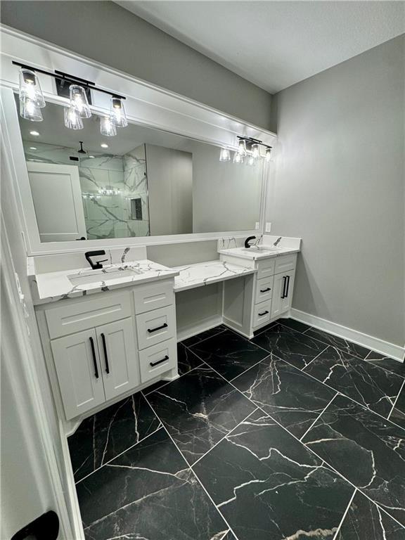 bathroom featuring a marble finish shower, baseboards, two vanities, and marble finish floor