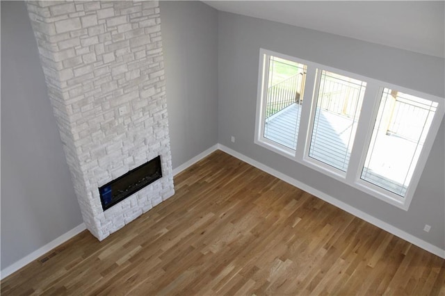 unfurnished living room with a fireplace, visible vents, baseboards, and wood finished floors