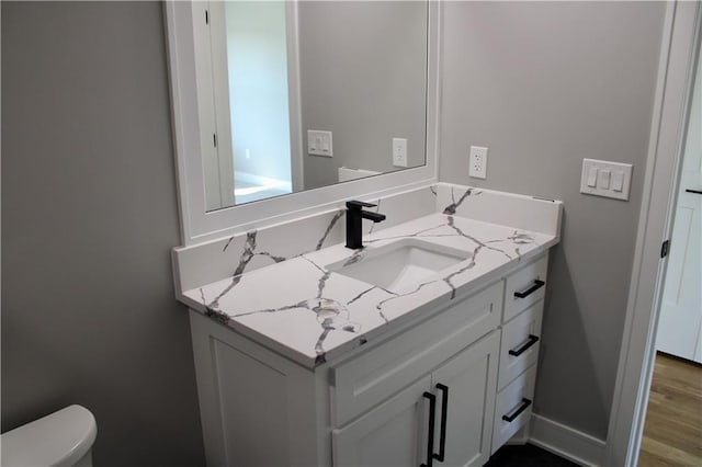 half bath with toilet, wood finished floors, vanity, and baseboards
