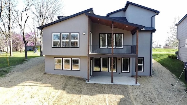 rear view of house with a patio, a balcony, stucco siding, and dirt driveway