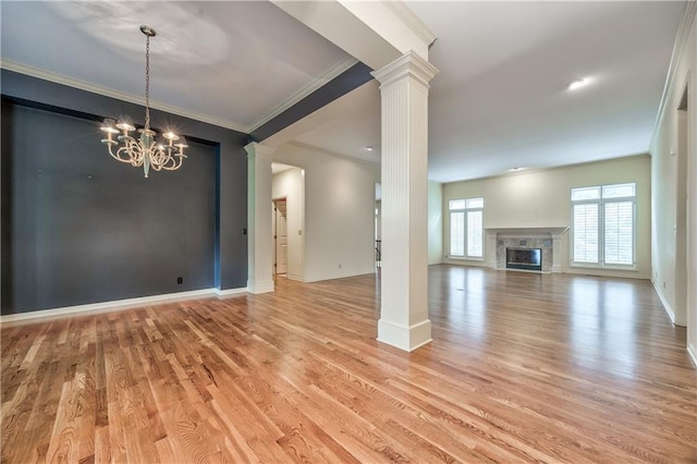 unfurnished living room with ornate columns, ornamental molding, light wood-type flooring, a high end fireplace, and a chandelier