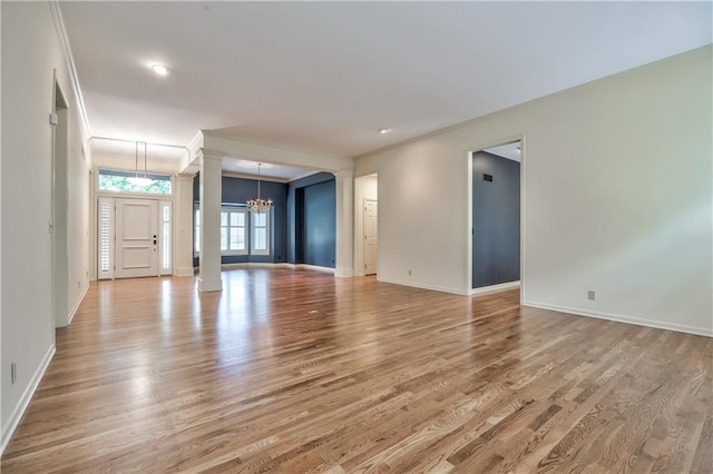 unfurnished living room featuring a chandelier, ornate columns, light wood-type flooring, baseboards, and ornamental molding