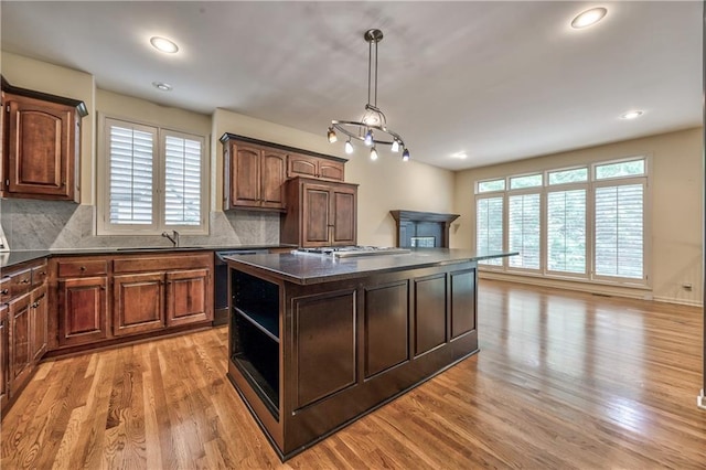 kitchen with dark countertops, dishwashing machine, a sink, light wood finished floors, and a center island