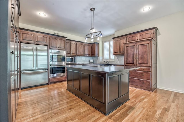 kitchen featuring built in appliances, dark countertops, light wood-style floors, a kitchen island, and hanging light fixtures