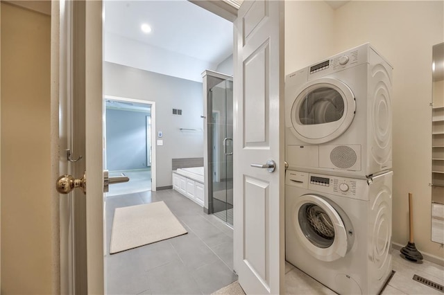 washroom with stacked washer / dryer, light tile patterned floors, and baseboards