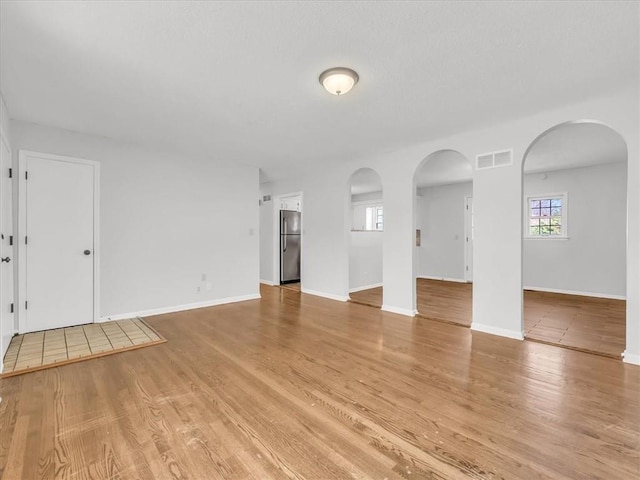 unfurnished living room with light wood-type flooring, baseboards, visible vents, and arched walkways