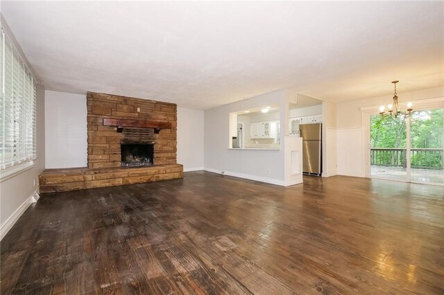 unfurnished living room with baseboards, a chandelier, a fireplace, and dark wood finished floors