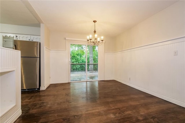 unfurnished dining area featuring dark wood-type flooring, a notable chandelier, and wainscoting