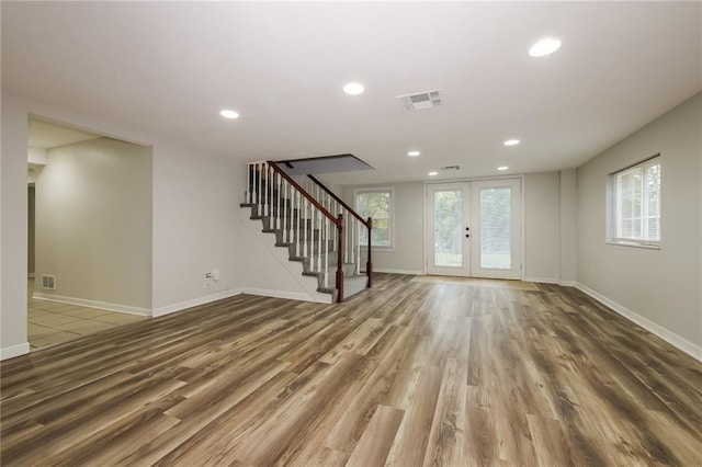 unfurnished living room featuring plenty of natural light, wood finished floors, visible vents, and stairs