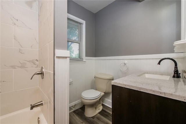 full bath featuring toilet, vanity, wood finished floors, a wainscoted wall, and bathing tub / shower combination