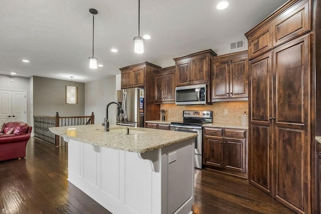 kitchen featuring a breakfast bar, a sink, stainless steel appliances, dark wood-type flooring, and a center island with sink