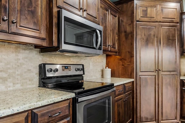 kitchen with backsplash, stainless steel appliances, light stone counters, and dark brown cabinets