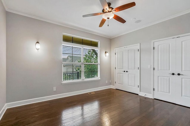 unfurnished bedroom featuring multiple closets, ornamental molding, baseboards, and wood finished floors