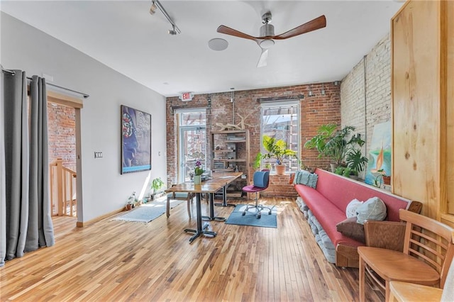 interior space with track lighting, light wood-style flooring, ceiling fan, and brick wall