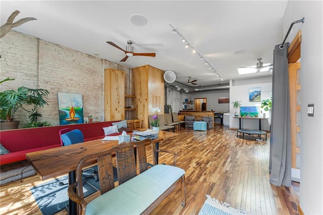 dining room with ceiling fan, rail lighting, hardwood / wood-style flooring, and brick wall
