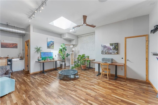 interior space with light wood-style floors, ceiling fan, rail lighting, a skylight, and baseboards