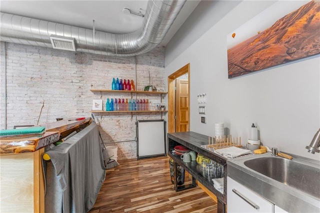 kitchen featuring a sink, visible vents, wood finished floors, and brick wall