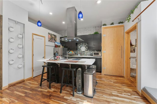 kitchen with tasteful backsplash, light countertops, light wood finished floors, and island exhaust hood