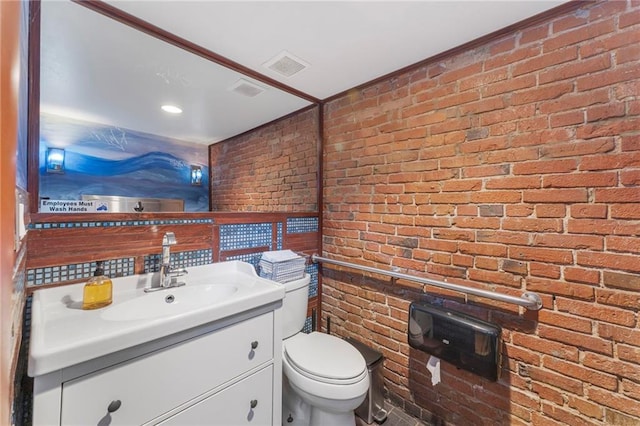 half bathroom featuring toilet, brick wall, vanity, and visible vents