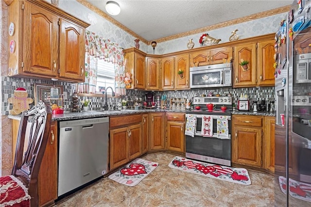 kitchen with decorative backsplash, a textured ceiling, appliances with stainless steel finishes, brown cabinets, and a sink