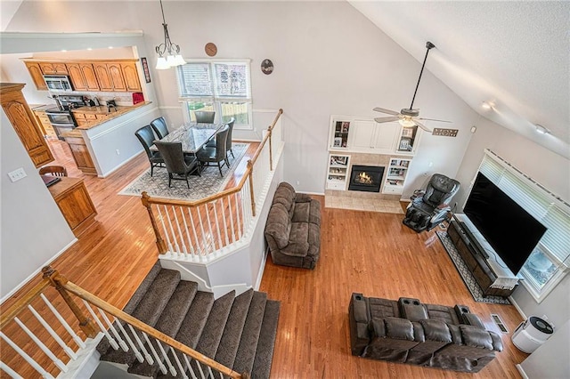 401 NW 51st St, Gladstone, MO 64118 - living room with a tiled fireplace, light wood finished floors, ceiling fan, high vaulted ceiling, and stairway