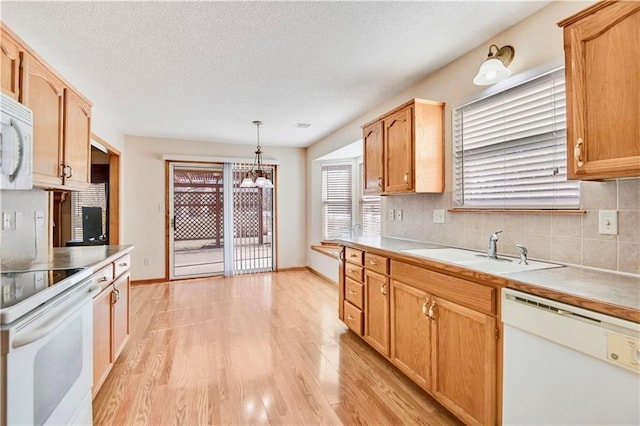 kitchen featuring white appliances, a sink, decorative backsplash, light wood-style flooring, and a chandelier