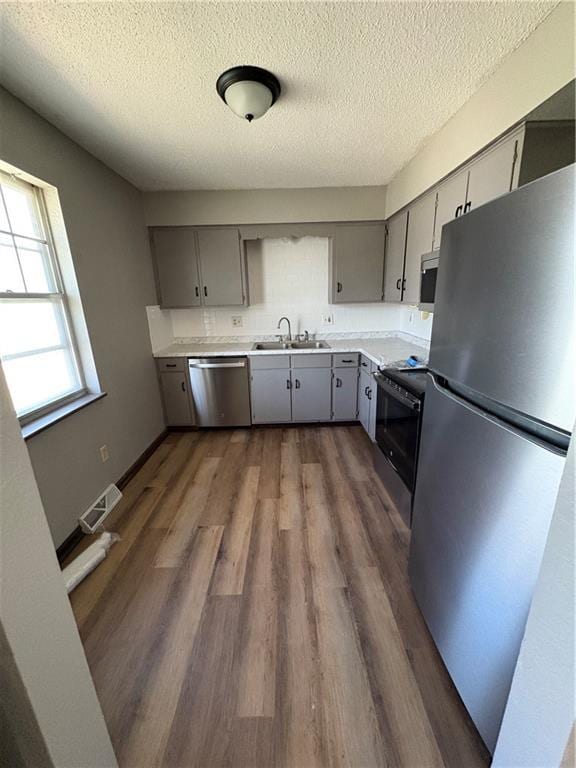 kitchen with a textured ceiling, appliances with stainless steel finishes, dark wood finished floors, gray cabinetry, and a sink