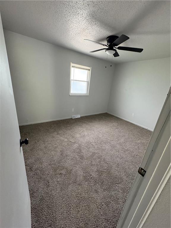 empty room featuring carpet floors, visible vents, baseboards, a textured ceiling, and a ceiling fan
