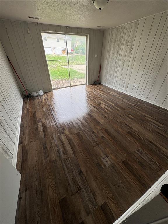 empty room featuring wood walls, a textured ceiling, and hardwood / wood-style floors
