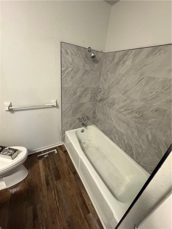 full bath with shower / washtub combination, toilet, wood finished floors, and visible vents