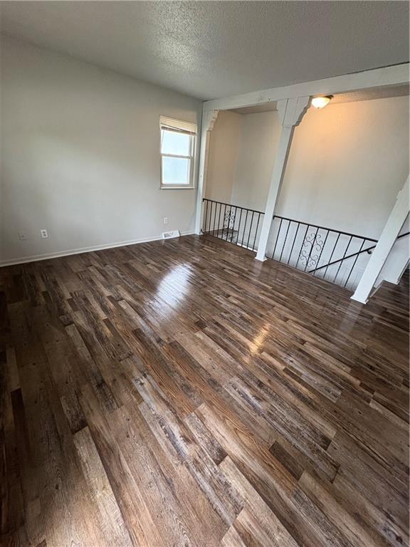 empty room featuring baseboards, a textured ceiling, wood finished floors, and visible vents