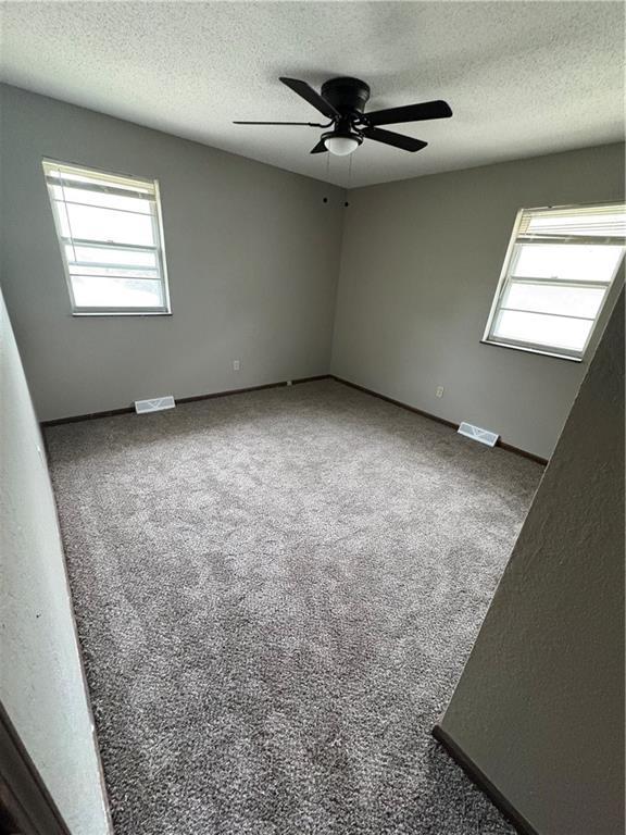 unfurnished room featuring ceiling fan, a wealth of natural light, a textured ceiling, and visible vents