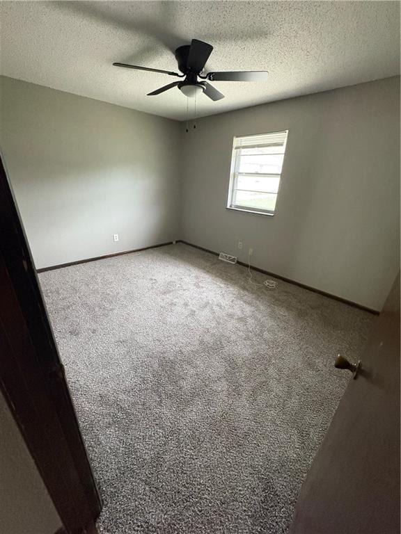 carpeted empty room featuring baseboards, ceiling fan, a textured ceiling, and visible vents