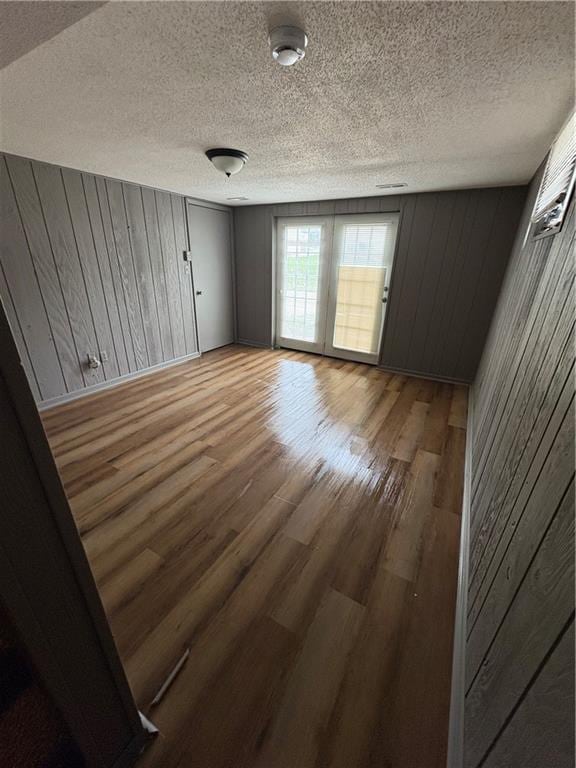empty room with light wood-type flooring, wood walls, and a textured ceiling