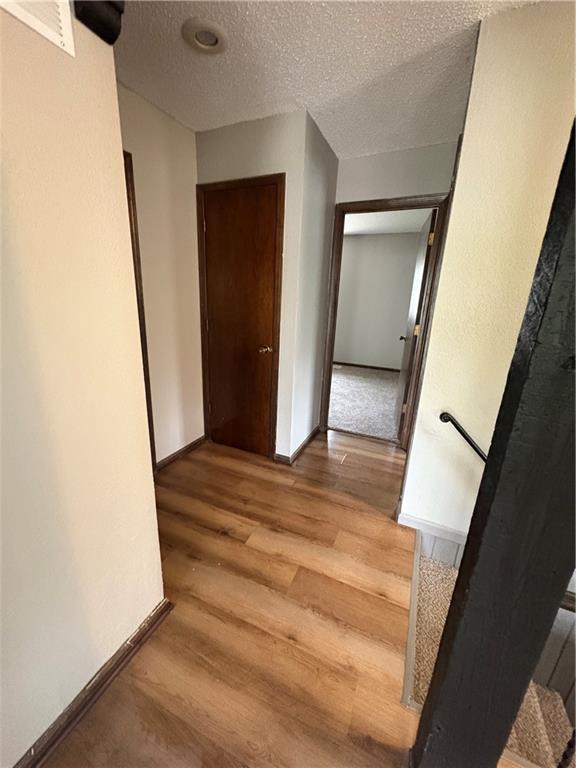 hall featuring light wood-style floors, baseboards, a textured ceiling, and visible vents