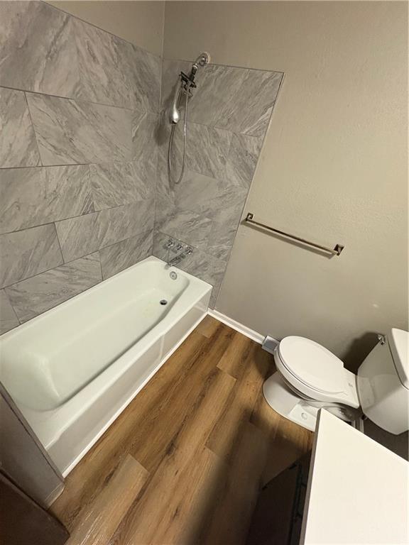 bathroom featuring baseboards, wood finished floors, toilet, and shower / washtub combination