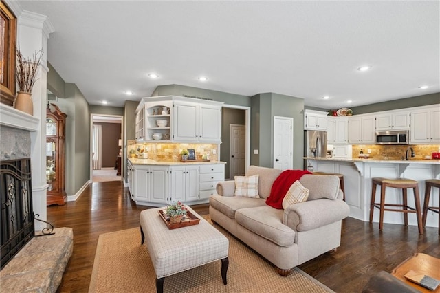 living area with recessed lighting, a fireplace with raised hearth, baseboards, and dark wood-style floors