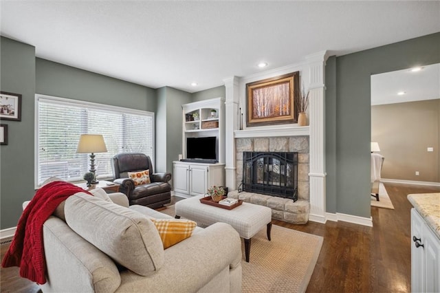 living room featuring baseboards, a stone fireplace, dark wood-style floors, recessed lighting, and built in shelves