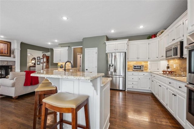 kitchen featuring a kitchen island with sink, white cabinets, dark wood finished floors, appliances with stainless steel finishes, and backsplash