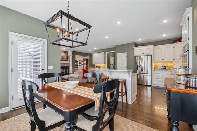 dining space with dark wood-style flooring, a toaster, a fireplace, recessed lighting, and a chandelier