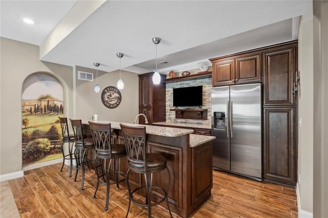 kitchen featuring stainless steel fridge with ice dispenser, a breakfast bar area, light wood finished floors, and visible vents