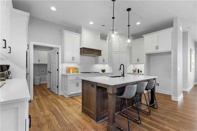 kitchen with custom exhaust hood, white cabinetry, a sink, and cooktop