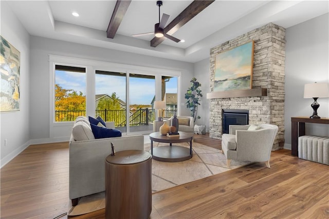 living area featuring ceiling fan, beamed ceiling, a fireplace, wood finished floors, and baseboards