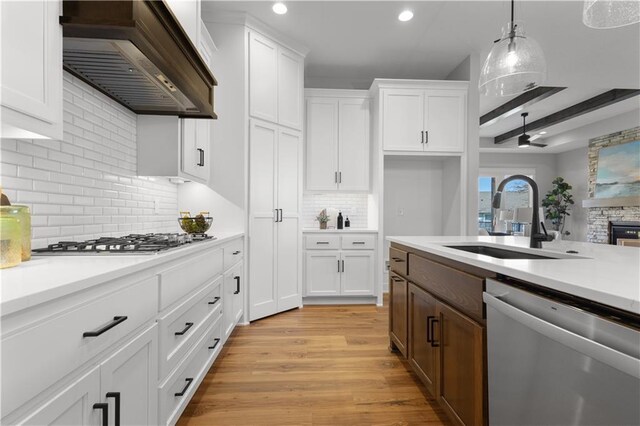 kitchen with custom exhaust hood, light countertops, white cabinets, stainless steel appliances, and a sink