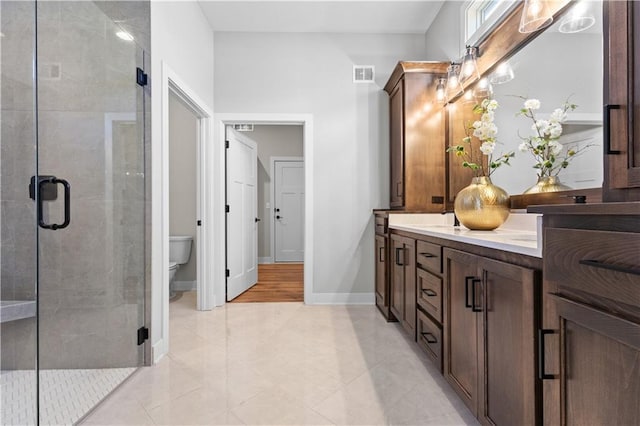 bathroom with a shower stall, visible vents, toilet, double vanity, and baseboards